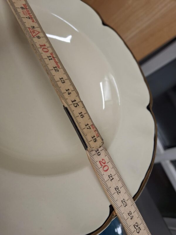 Nærbillede af en dyb tallerken fra Johnson Bros. 'Virtorian Cream' med guldkant, der viser en tommestok, der indikerer en diameter på ca. 19 cm, og fanger detaljerne i den bølgede kant.