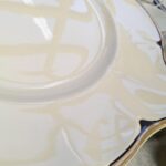 Nærbillede af kanten på et 'Victorian' fad fra Johnson Bros., der tydeligt viser den skinnende guldkant og de mørkeblå, næsten sorte, detaljer på den cremede porcelænsoverflade.