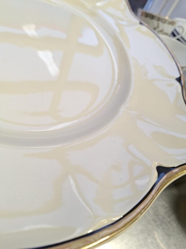 Nærbillede af kanten på et 'Victorian' fad fra Johnson Bros., der tydeligt viser den skinnende guldkant og de mørkeblå, næsten sorte, detaljer på den cremede porcelænsoverflade.