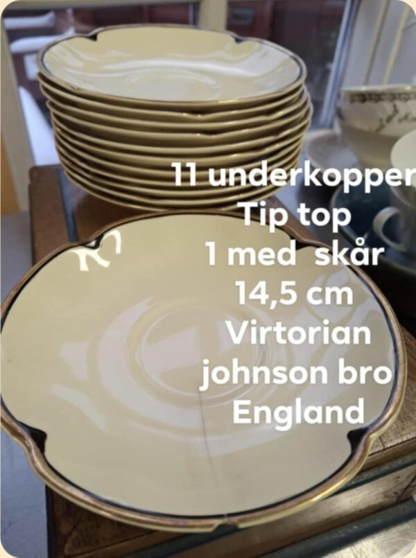 En enkelt cremehvid Johnson Bros. 'Victorian' underkop med guldkant, der er placeret foran en stabel lignende underkopper. Der er tekst på billedet, der angiver antal, mål og mærke, samt info om et skår.