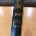 Bogryg 'Farlig Kyst' med flyillustration og guldpræg
