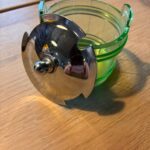 Åben grøn glasbeholder med skinnende sølvlåg på træbord