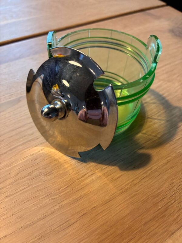 Åben grøn glasbeholder med skinnende sølvlåg på træbord