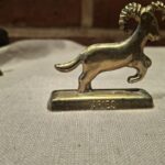 Messingfigur af vædder på beige klæde