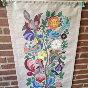 Farverigt vægtæppe med fuglemotiv mod murstensvæg