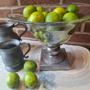 Glasopsats med limefrugter og metalfod på hvid dug