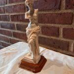 Venus de Milo statue i cremehvid med brun fod mod murstensbaggrund