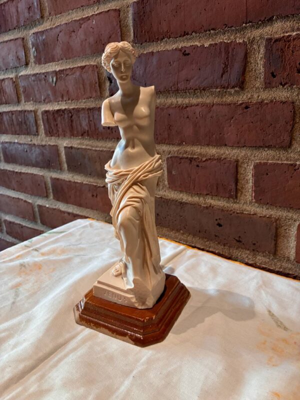 Venus de Milo statue i cremehvid med brun fod mod murstensbaggrund