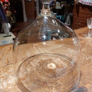 En klar glaskuppel med en rund knop på toppen, stående på et rustikt træbord indendørs i dæmpet belysning.