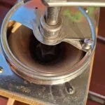 Nærbillede af toppen af en vintage kaffekværn i metal med brugsspor, der viser kværnemekanismen set indefra.