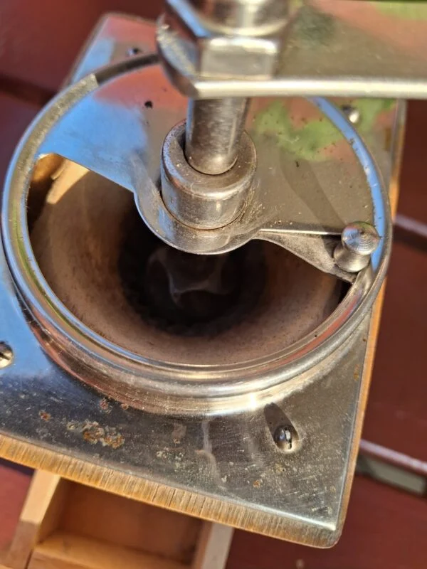 Nærbillede af toppen af en vintage kaffekværn i metal med brugsspor, der viser kværnemekanismen set indefra.