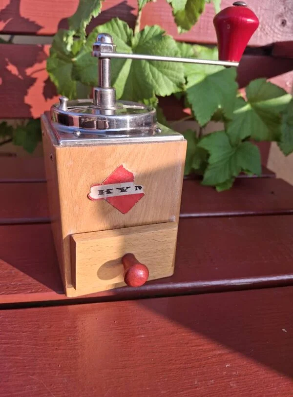 Gammel kaffekværn i lyst træ med metaltop, røde knopper og en delvist slidt etiket på fronten.