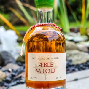 En flaske Ny Nordisk Mjød Æble Mjød 35 CL med grøn voksforsegling, placeret udendørs på en sten i sollys.