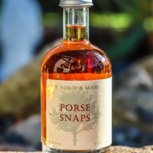 En flaske 'NY NORDISK MJØD PORSE SNAPS' på 5 cl med ravfarvet væske, placeret udendørs på en sten med sløret grøn baggrund.