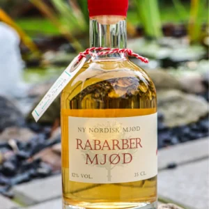 En flaske Ny Nordisk Mjød Rabarber Mjød 35 CL med rød voksforsegling, placeret på en sten udendørs i sollys.