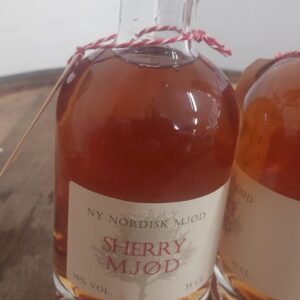 To flasker 'NY NORDISK MJØD SHERRY MJØD' på 35 cl med gyldenbrun væske og rød vokslignende forsegling, på en træoverflade.