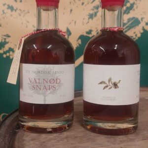 To små flasker 'NY NORDISK MJØD VALNØD SNAPS' op 5 cl med brunlig væske og rød vokslignende forsegling, på en træoverflade.