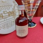 Hvid platte med gyldent motiv af en mand ved en maskine, sammen med et glas og en flaske blåbærmjød.
