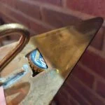 Nærbillede af en kapsel i åbningen på en trekantet øloplukker med gullig metaloverflade og synlige brugsspor.