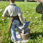 Bagsiden af porcelænsfiguren "Smeden", der viser figuren i hvid trøje og gråt forklæde, stående ved en ambolt i græsset.