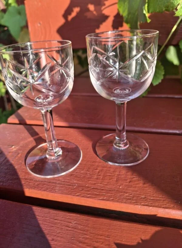 To klare glas på fod med skrå linjer i mønstret, fotograferet sammen på en rød træbænk.