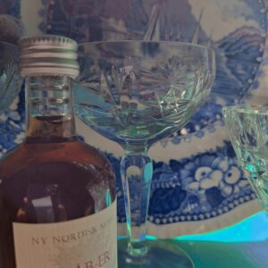 Et nærbillede af et smukt skåret krystalglas, der reflekterer lys i blå nuancer. Synlig traditionel blå og hvid platte i baggrunden.