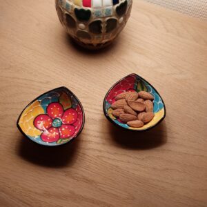 Nærbillede af to farverige, håndmalede tapasskåle, den ene med mandler, med en mosaiklampe i baggrunden.