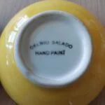 Bunden af en gul håndmalet tapasskål fra 'Del Rio Salado', hvor teksten 'HAND PAINT' er synlig.