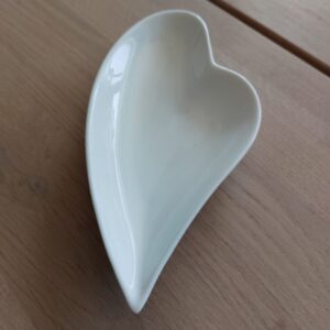Et lille, hvidt hjerteformet fad i keramik, placeret på en lys træoverflade.