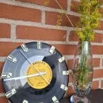 VillaSnaks hjemmelavede ur af en LP-plade med dominobrikker som timemarkører; vase og blomster står ved siden af.