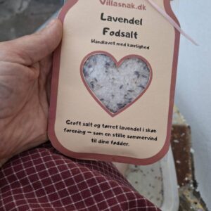 En hånd holder en pose 'Lavendel Fodsalt' fra Villasnak.dk, med en hjerteudskæring, der viser saltet.