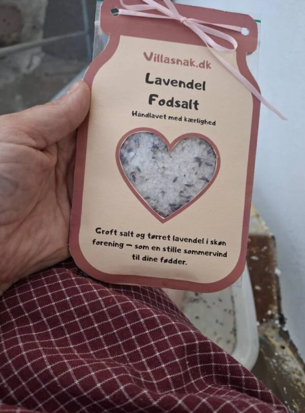 En hånd holder en pose 'Lavendel Fodsalt' fra Villasnak.dk, med en hjerteudskæring, der viser saltet.