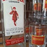 Et nærbillede af en Beefeater London Dry Gin flaske og to matchende gin glas med logo, på træbord.