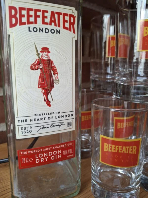 Et nærbillede af en Beefeater London Dry Gin flaske og to matchende gin glas med logo, på træbord.