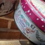 Siden af en lille rund vintage Quality Street dåse med et julemotiv af en soldat og julepynt.