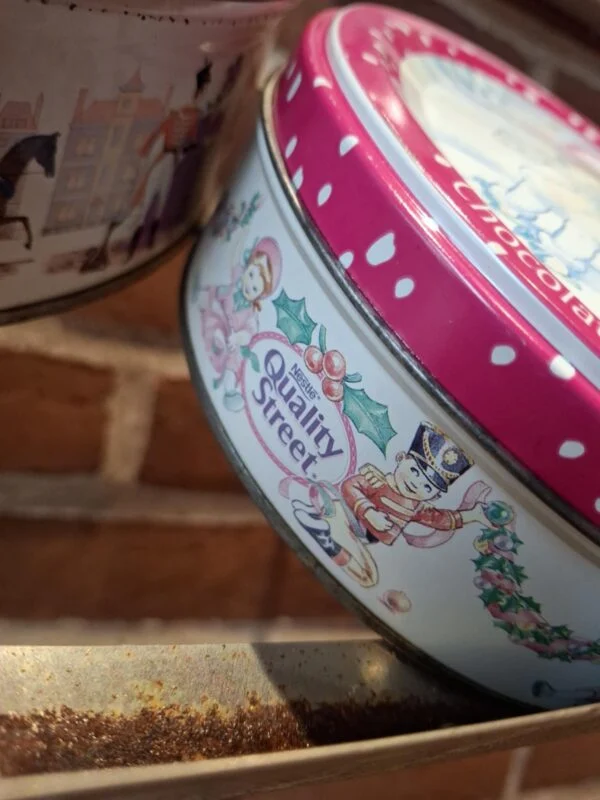 Siden af en lille rund vintage Quality Street dåse med et julemotiv af en soldat og julepynt.
