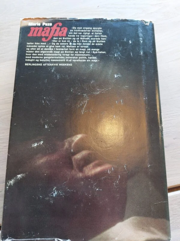 Bagsiden af bogen 'Mafia' af Mario Puzo med en mørk baggrund og tekst om bogen.