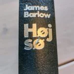 Ryggen af bogen 'Høj sø' af James Barlow med sølvfarvet tekst på mat sort omslag.