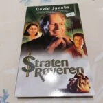 Forsiden af bogen 'Stratenrøveren' af David Jacobs, med billeder af skuespillere og pengesække.