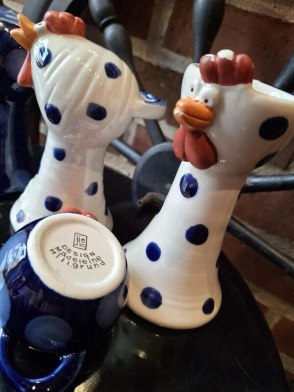 Bundstempel på en blå keramikhøne med Jie og Design Madeleine Hillgrund. Hvide høns med blå prikker står bagved.
