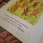 Et opslag fra bogen 'Palle P' med farverige illustrationer af en gruppe brune kaniner, der hopper og danser på en grøn plæne.