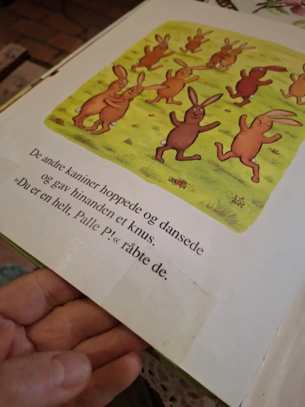 Et opslag fra bogen 'Palle P' med farverige illustrationer af en gruppe brune kaniner, der hopper og danser på en grøn plæne.
