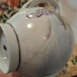 Nærbillede af en kandes side med figurmotiv og tydelige mørke, forgrenede revnelignende linjer i overfladen.