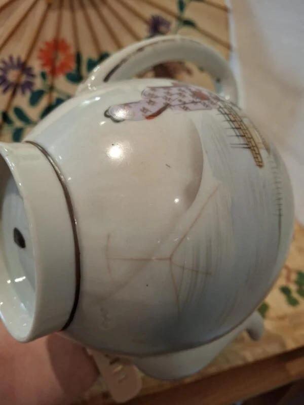 Nærbillede af en kandes side med figurmotiv og tydelige mørke, forgrenede revnelignende linjer i overfladen.
