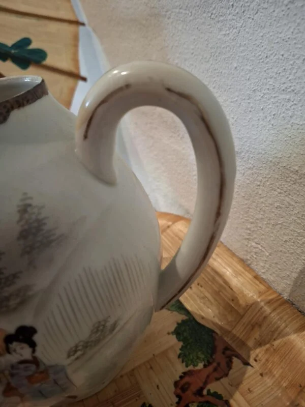 Nærbillede af en lys kandes buede hank med slid i den gyldne kant og dele af et figurmotiv.