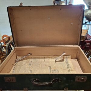 En åben mørkegrøn vintage Vulkolit rejsekuffert med brunt interiør og avispapir i bunden, set fra oven.