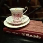 Bogen 'Tid til at elske' af Lilli Palmer ligger under et elegant hvidt tesæt med lyserøde roser og guldkant.