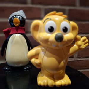 To vintage sparebøsser: en pingvin med grå hue og rød halstørklæde, og en gul, vinkende figur.