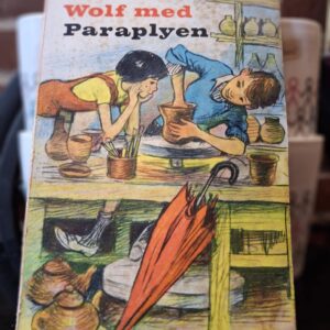 Bogomslag af 'Wolf med Paraplyen' af Ilse Kleberger, der viser to børn i gang med at dreje keramik, med en orange paraply i forgrunden.