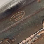 Nærbillede af mærkets logo 'Vulkolit - Dansk Arbejde' på en patineret mørkegrøn vintage rejsekuffert.